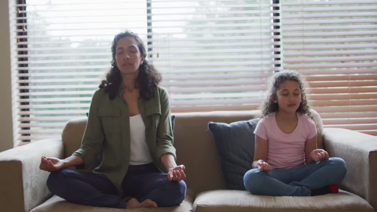 madre e hija de raza mixta meditando en la sala de estar
