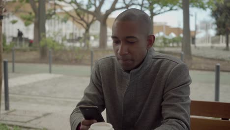 man holding paper cup and using smartphone on street