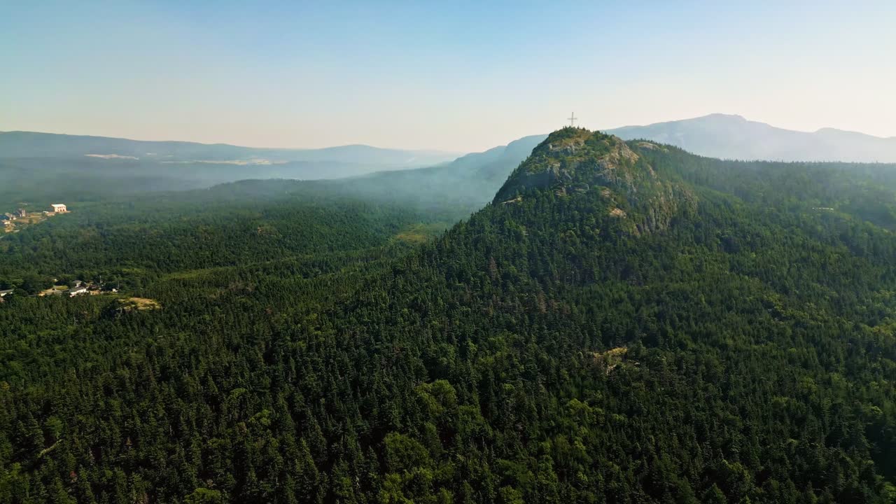 A drone glides over Holyrood, capturing smoke rising above forested hills and rolling terrain with glimpses of the ocean on Newfoundland’s coast