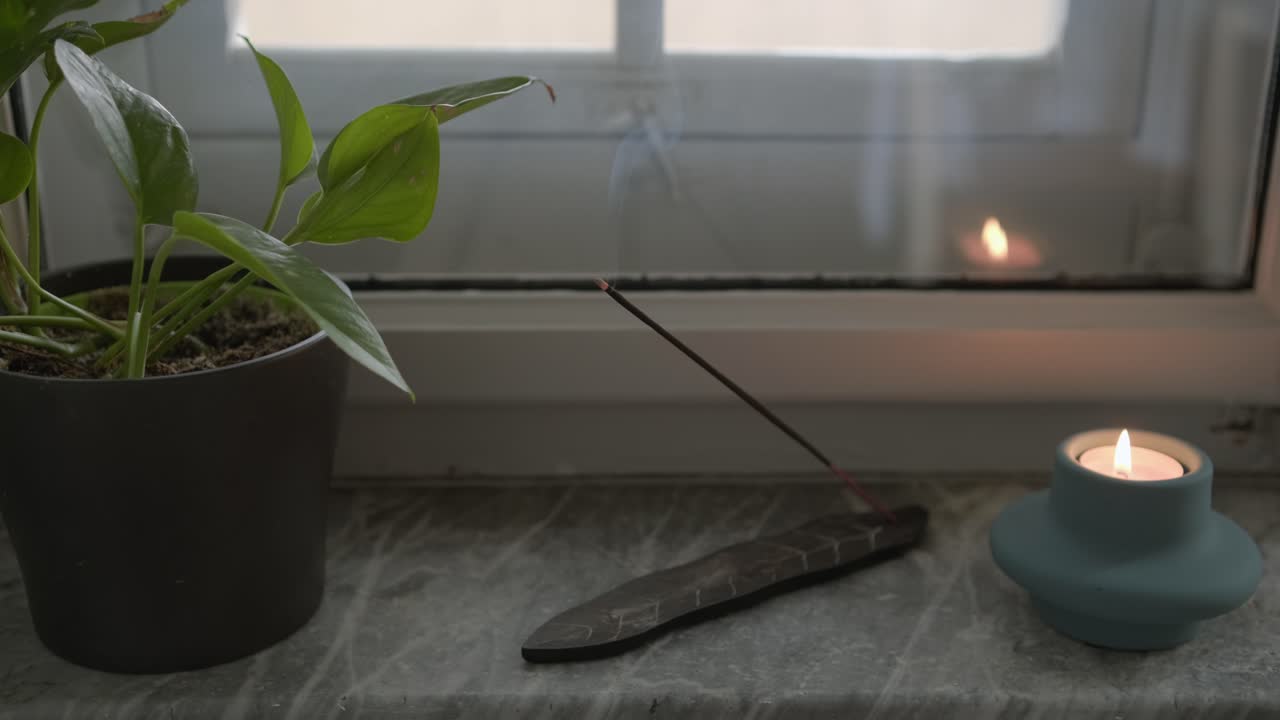 Fumée d'un bâton d'encens et bougie relaxante près de la fenêtre du salon, rituel de yoga et de méditation