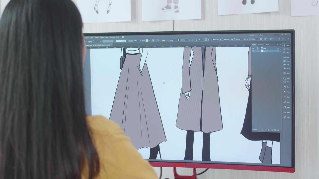 여성 디자이너가 스튜디오의 데스크에서 옷을 디자인하는 어깨를 통해 볼 수 있습니다. 옷 제작 절차 개념. 사이버 게임 옷과 디자인.