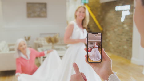 grandmother with adult daughter and granddaughter trying on wedding dress taking picture on phone