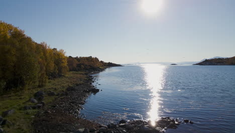 clean and serene ocean water by the coast of senja island in sunset - aerial shot