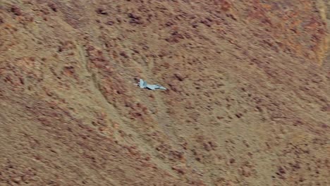 Slow-motion,-close-up-view-of-a-fighter-jet-flying-low-in-a-colorful-canyon-and-exiting-over-a-valley
