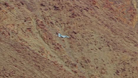 cámara lenta, vista de primer plano de un avión de combate volando bajo en un cañón colorido y saliendo sobre un valle