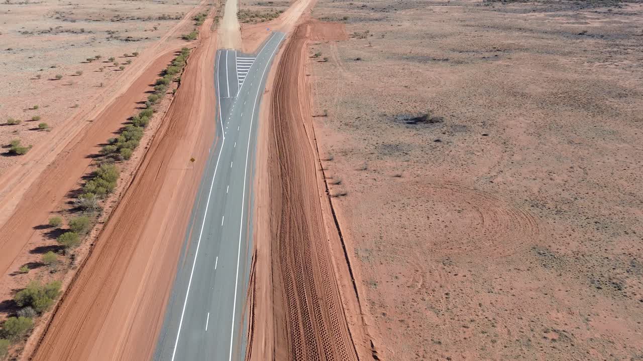 Watch as the sealed road disappears into red dirt, marking the gateway to the true Australian outback—raw, remote, and untamed