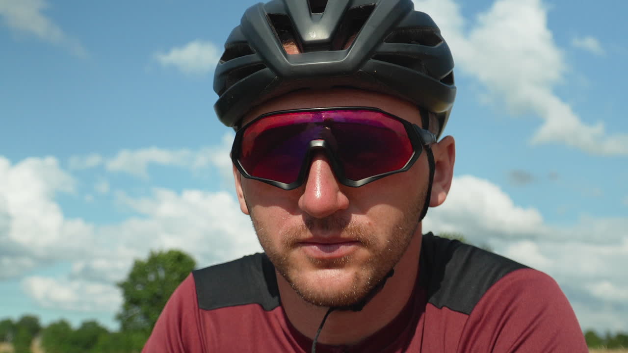 ciclista caucásico enfocado hombre con gafas deportivas y casco prepárate para comenzar la carrera de entrenamiento en bicicleta - contra el cielo nublado en un día de verano retrato de cerca cara