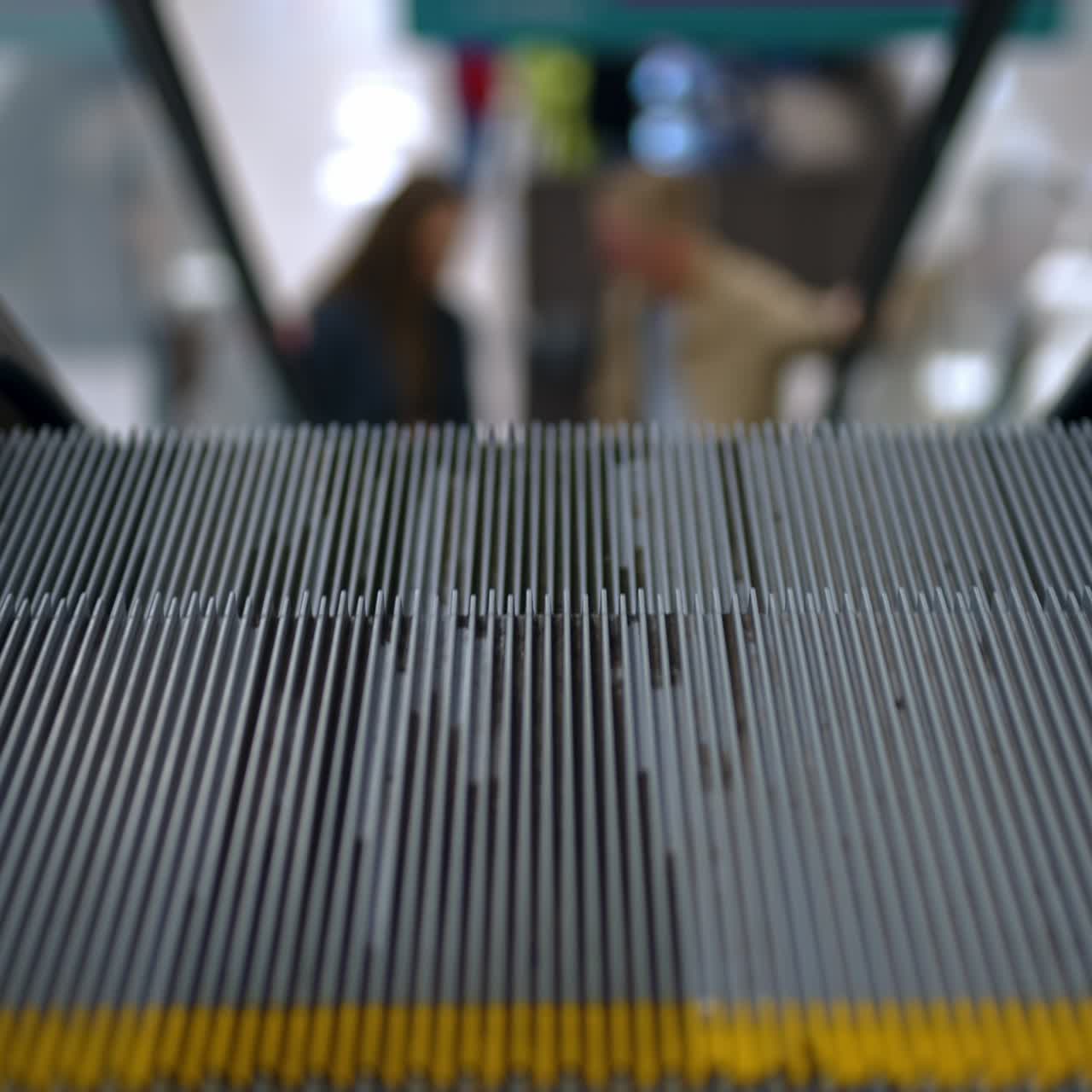 Metal steps of escalator moving quickly. Close up. A couple rising by the escalator in the mall. Blurred backdrop