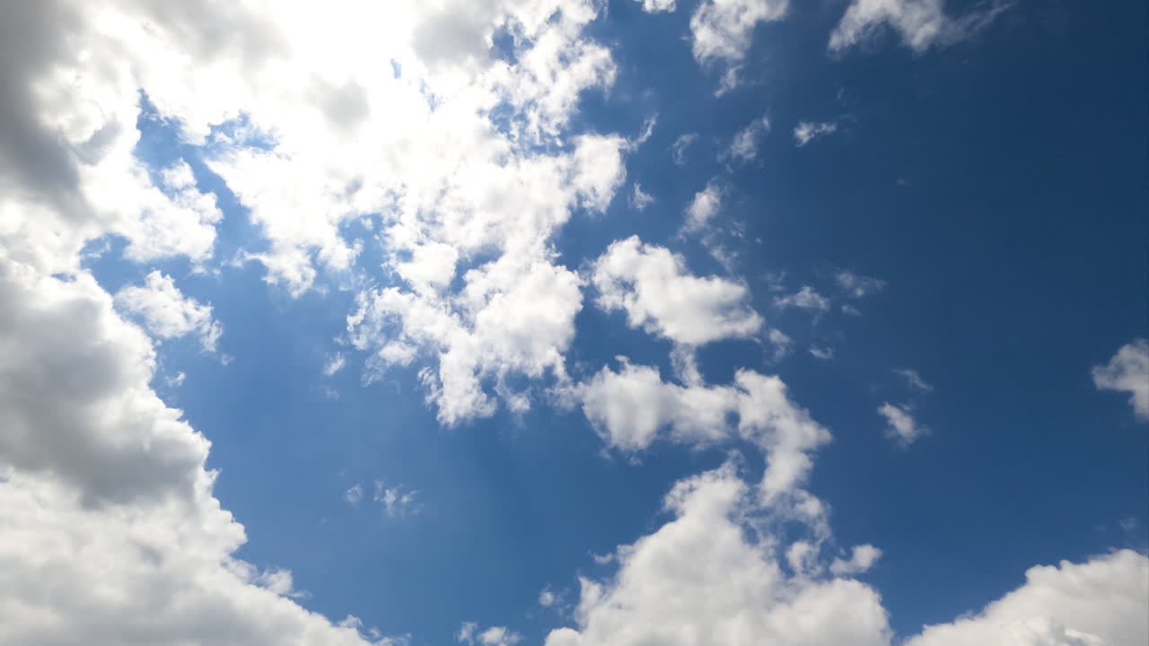 White puffy clouds flying through against the shining sun. Cumulus clouds gathering into a grey cloudscape timelapse. View from below.