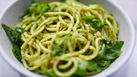 spaghetti and pesto with rocket and pinenuts rotating in a bowl