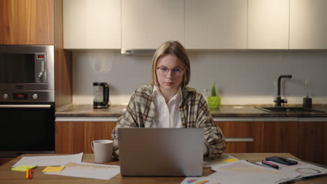 mature businesswoman working from home focused woman is working with her laptop and paper documents sitting in the kitchen at home. laptop app calculate costs expenses estimate budget for project