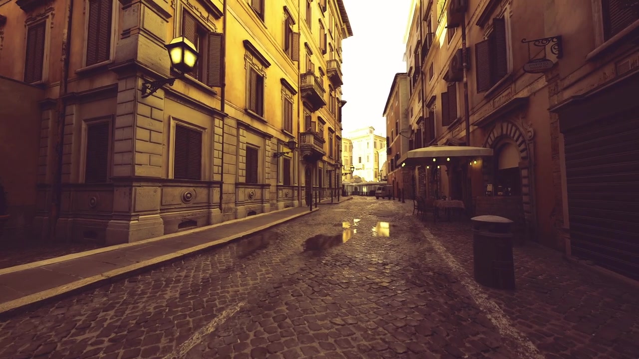 Vicolo bagnato dalla pioggia illuminato da luci calde dei negozi e figure distanti.