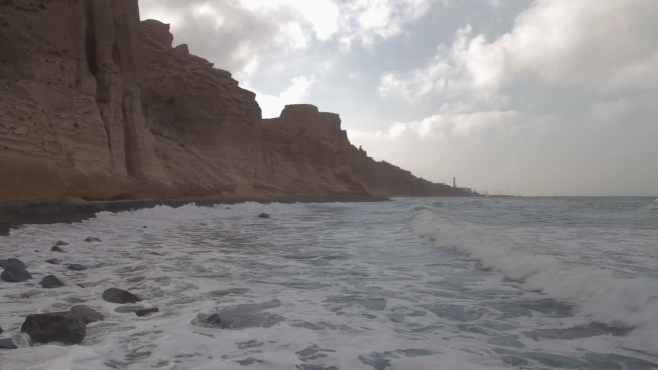 Waves hitting a black sand beach surrounded by white volcanic cliff formations