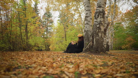 novelist enjoying book in solitude wears yellow beret scarf around neck, deeply focused on book in beautiful autumn park, surrounded by golden leaves and birch trees