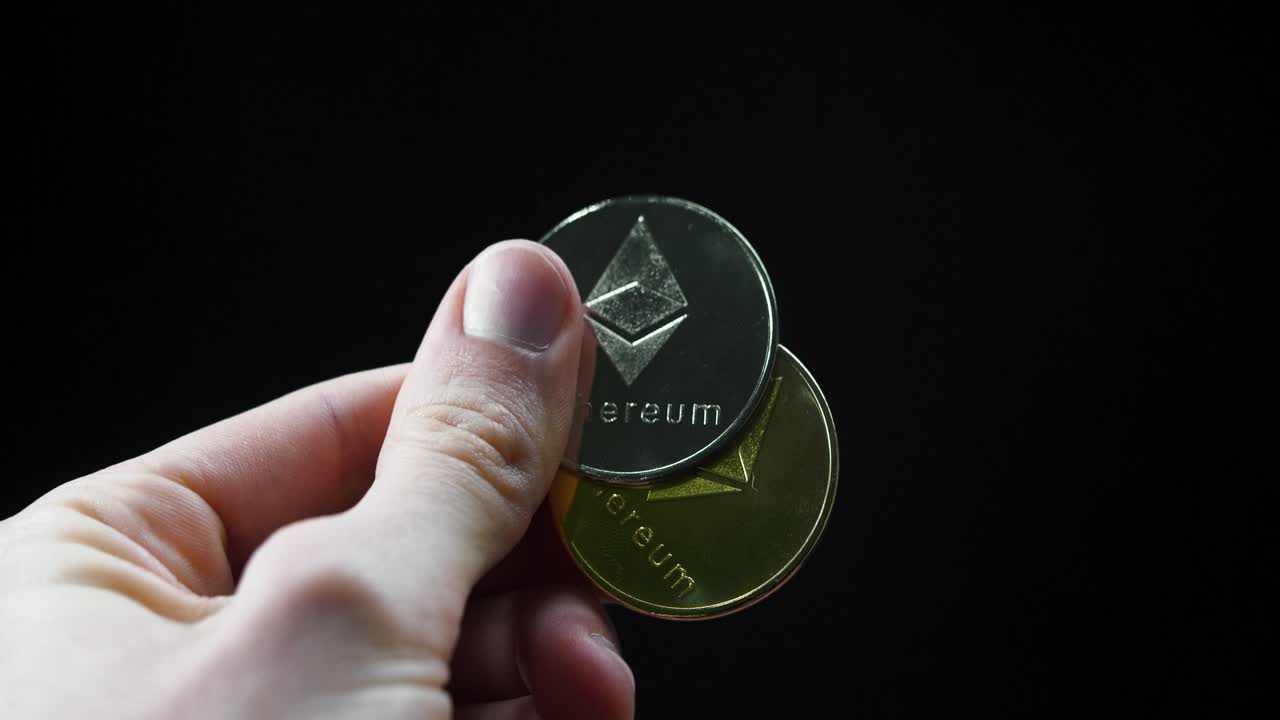 A close-up of a hand shifting gold and silver Ethereum coins, reflecting under light