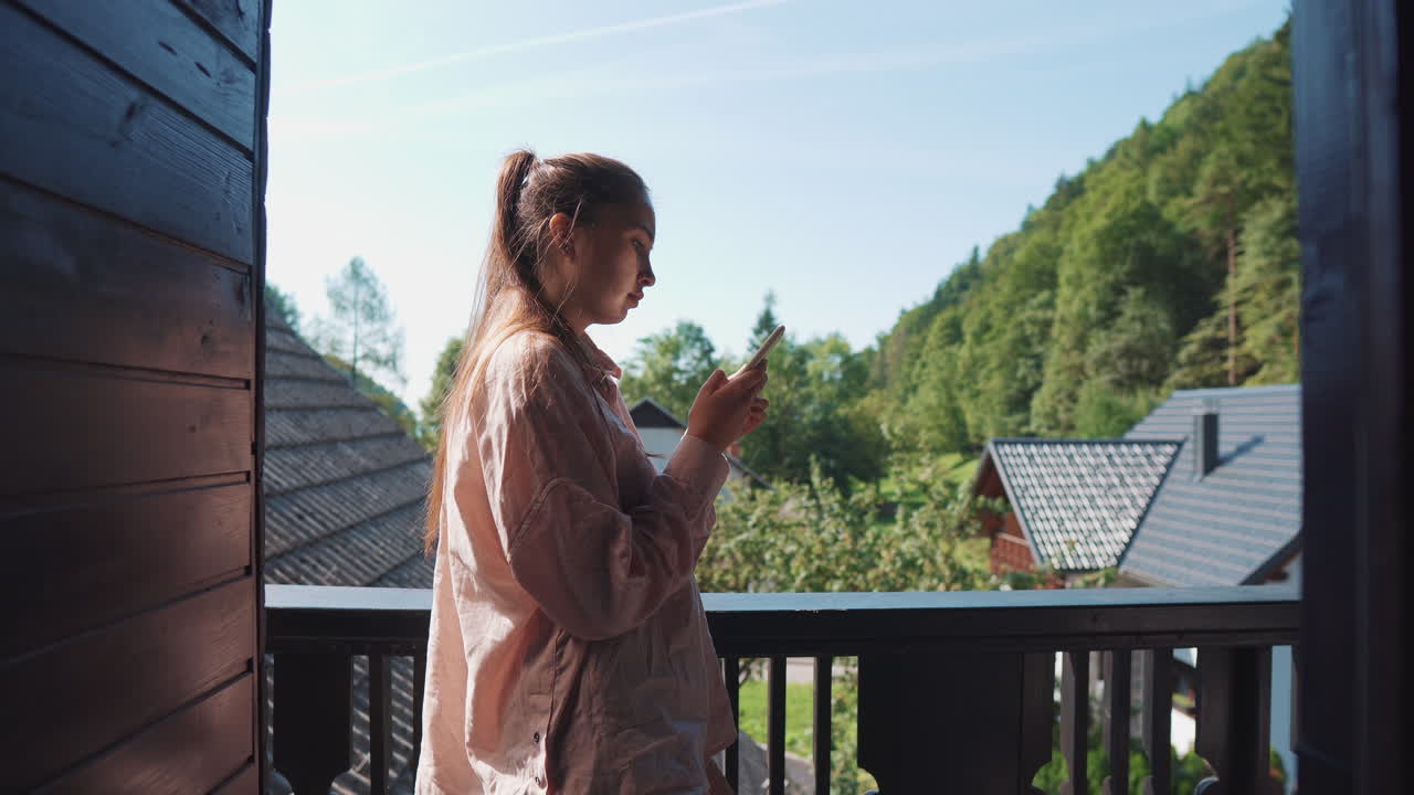 mujer joven usando un teléfono inteligente en un balcón con vistas a las montañas y la naturaleza