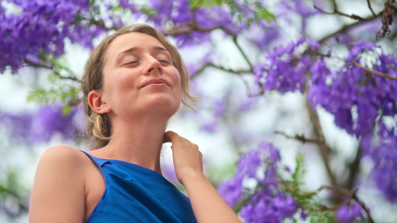 Caucasian woman in blue dress posing, tree with pink flowers in Barcelona, Spain