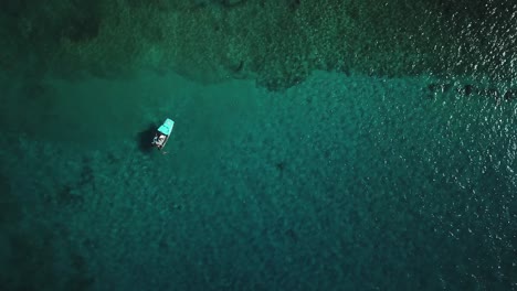 Vista-Aérea-Ascendente-De-Un-Barco-Que-Se-Relaja-Sobre-Un-Arrecife-De-Coral-Que-Se-Encuentra-En-Aguas-Cristalinas