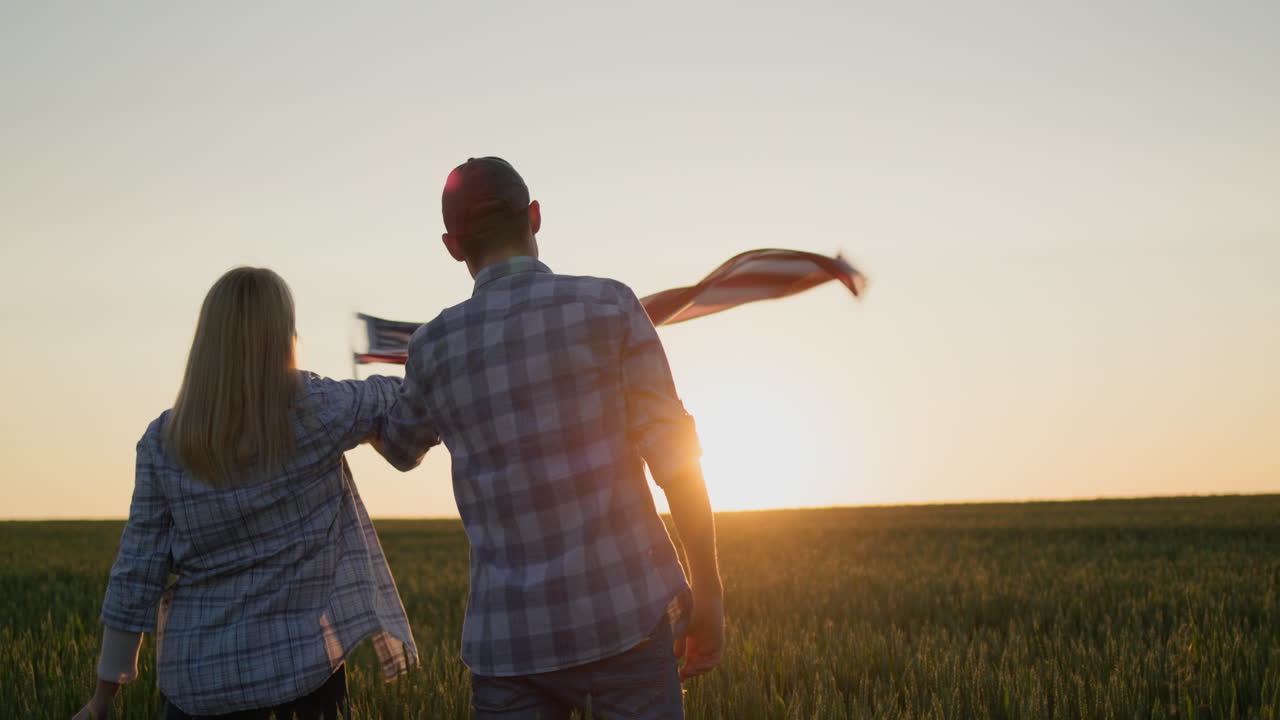 독립일을 축하하는 - 한 남자가 미국 발을 흔들고 있습니다. 해가 지는 밀의 배경에 서 있습니다.