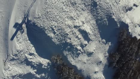 Aerial-top-down-of-fresh-white-snow-covered-mountains-peak-with-christian-cross,-trekking-adventure-winter-outdoor-ski-activity