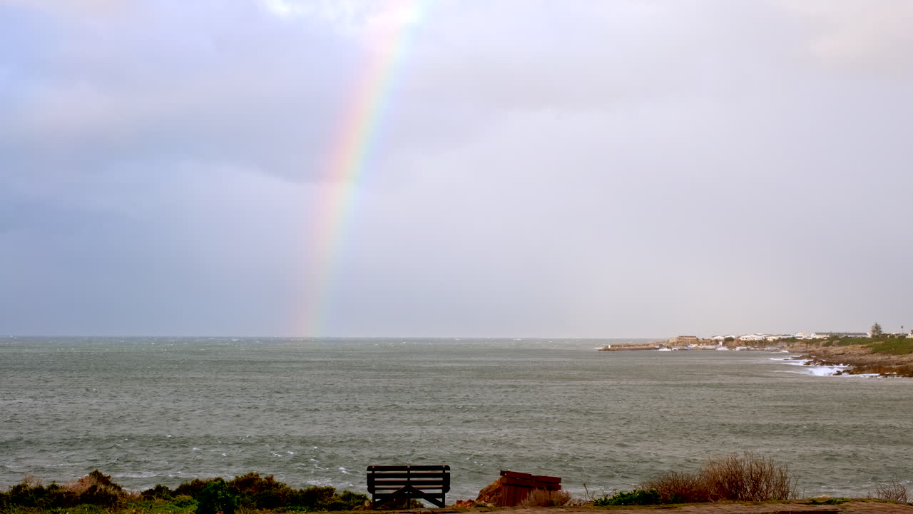 View from Hermanus coastline of rainbow over ocean on windy and stormy day