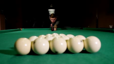 a brutal man with tattoos on his hands is playing russian billiards in a bar.