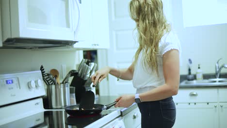 Handheld-slow-motion-shot-of-a-young-blonde-female-cooking-chicken-in-a-pan-over-a-stove