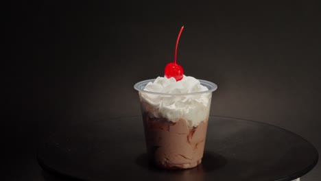 taza de crema de chocolate cereza parfait en la parte superior girando en la mesa giratoria con fondo negro