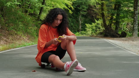 mujer usando el teléfono mientras está sentada en una patineta en el bosque
