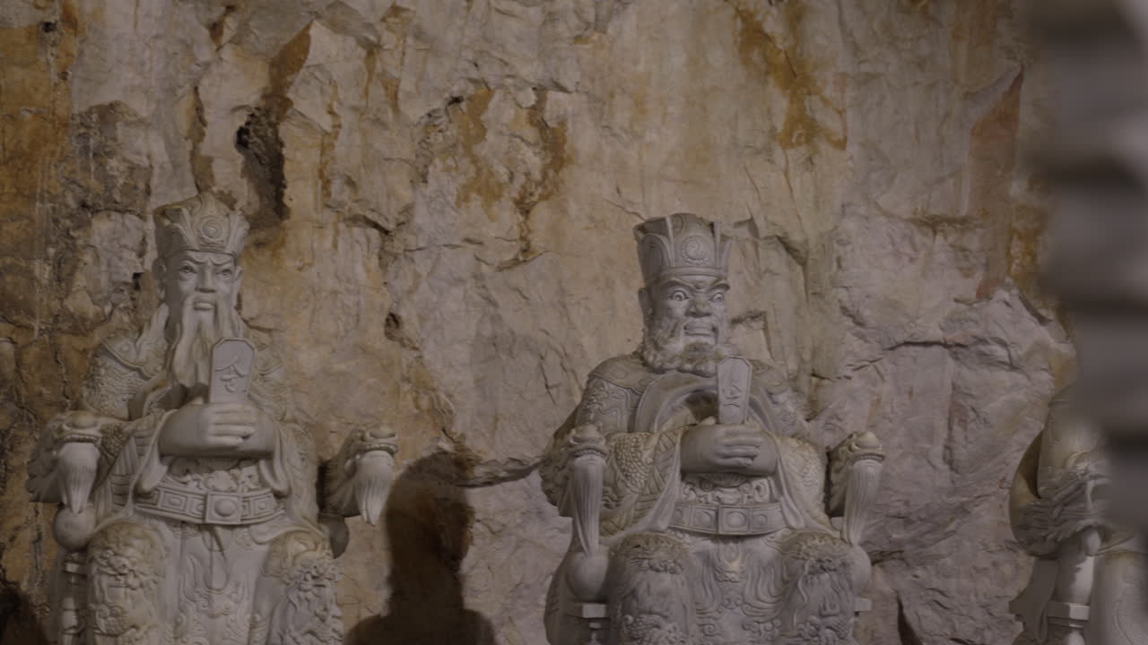 A group of stone statues depicting ancient kings, carved in a natural cave setting in Vietnam