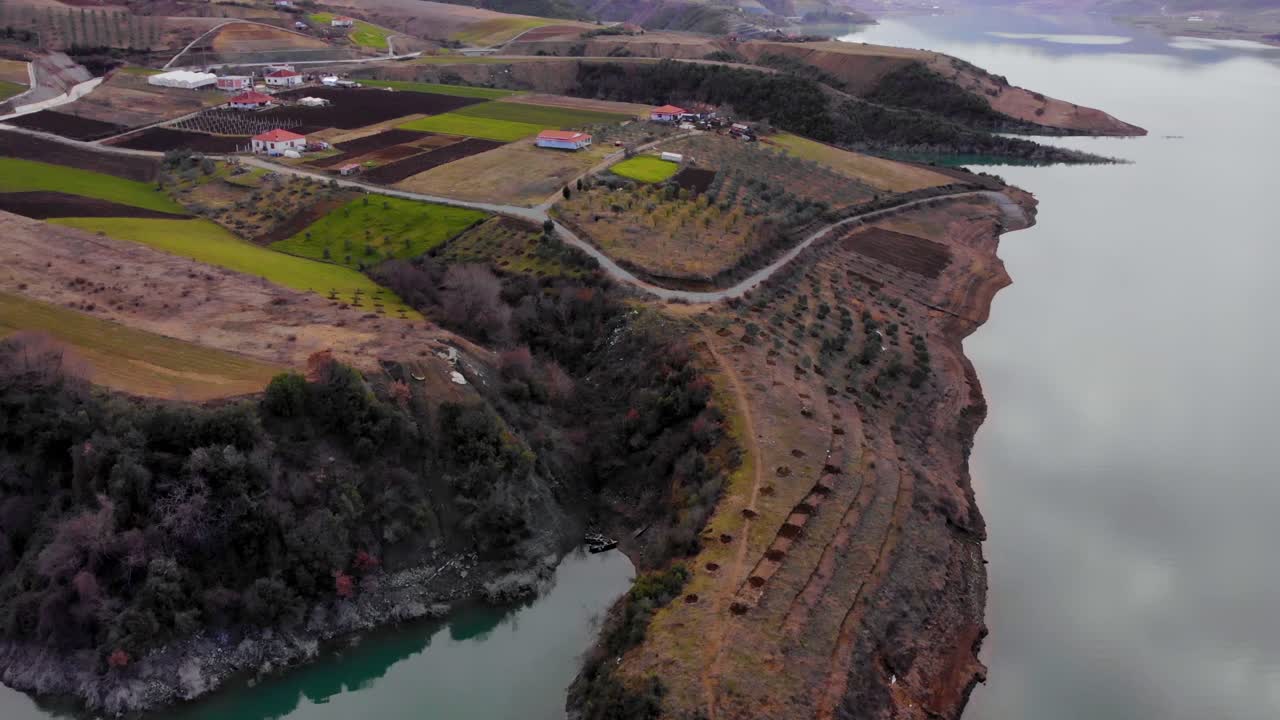겨울날 회색 구름을 반사하는 잔잔한 호수로 둘러싸인 언덕의 경사면에 있는 마을 주택과 다채로운 구획