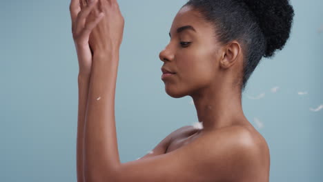 slow motion beauty portrait attractive african american woman feathers falling on smooth skin touching bare shoulders enjoying natural skincare gently caressing body in blue background