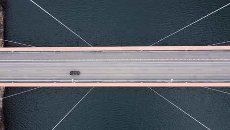 Spectacular-birdseye-view-over-Hardanger-suspension-bridge--Moving-sideways-over-road-with-wires-passing-close---From-middle-of-fjord-until-tunnel-entrance---Sea-Hardangerfjorden-seen-below