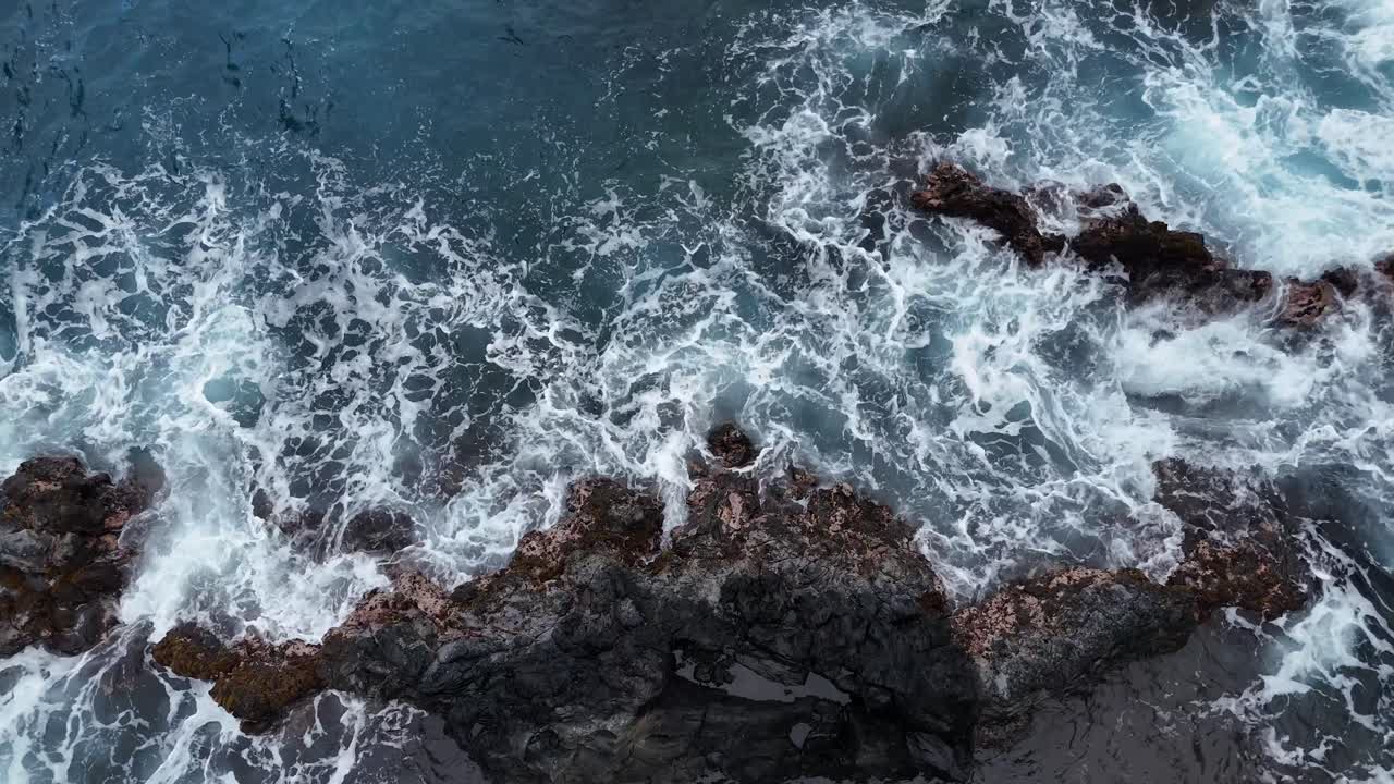 Vista a volo di drone dall’alto di onde che si infrangono su una roccia nera, creando spettacolari motivi di schiuma bianca. Potente movimento oceanico e straordinarie texture costiere a Hana, Maui, Hawaii