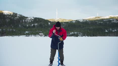 hombre perforar un agujero con una barrena en un lago congelado para la pesca en el hielo