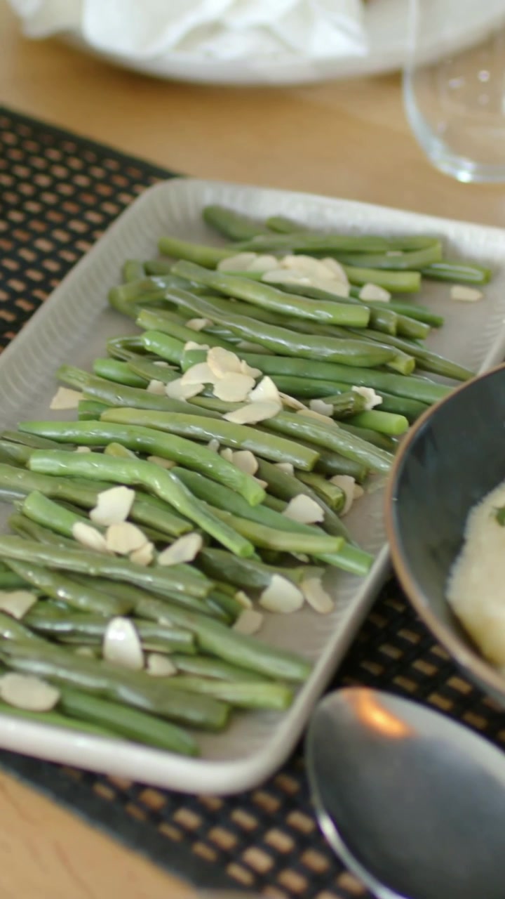 Vertical video: Panning camera over bean tray with almond at wood table, revealing mash, copy space