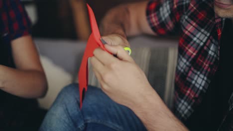 man is cutting heart from colored paper by scissors on valentine's day near sweetheart