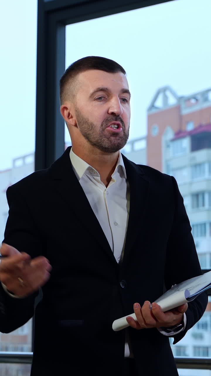 Middle-aged boss in suit standing in front of employees and holding papers. Man replying questions of his staff against city backdrop. Vertical video