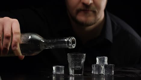 der barkeeper gießt gefrorenes wodka, sake aus der flasche in ein schlagglas mit eiswürfeln und trinkt