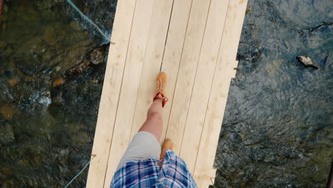 a woman walks along a narrow shaky bridge across a mountain river overcome the fear of concept pov v