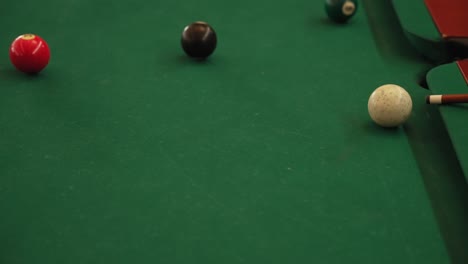 close up of billiard balls near pocket with cue stick on green felt table surface