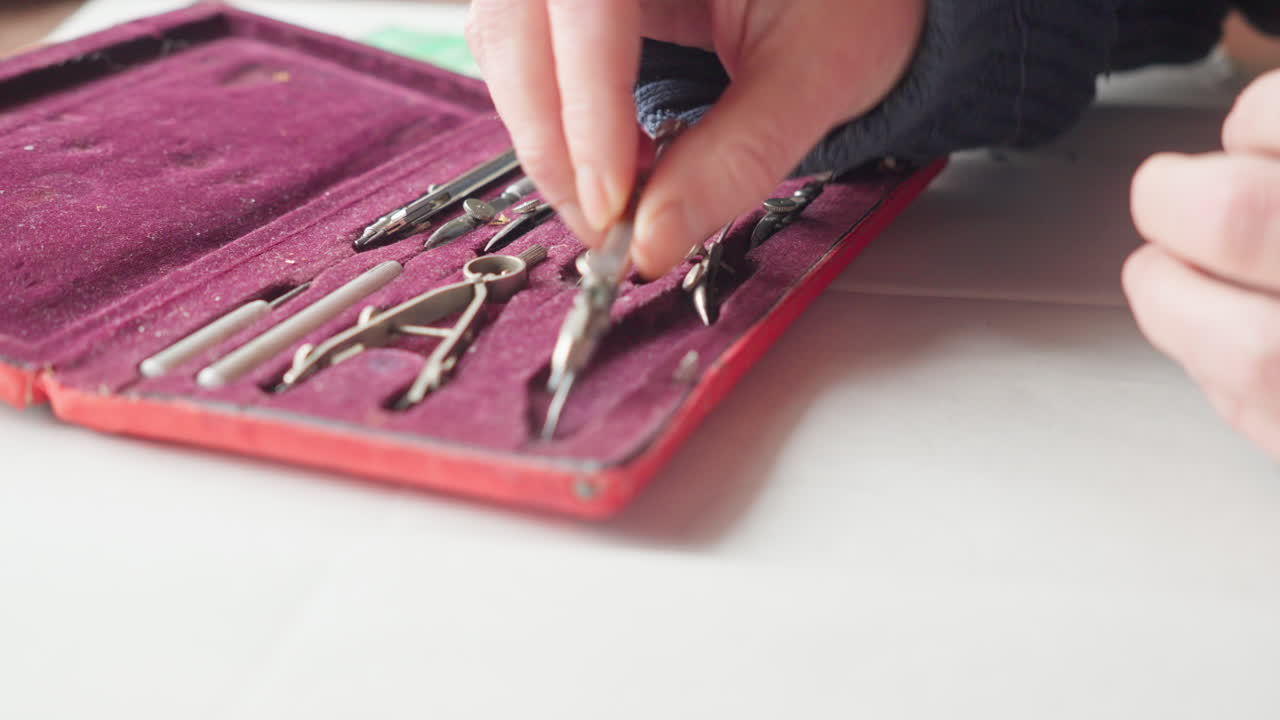 Close-up of hands carefully placing drafting tools back into a fitted case, suggesting discipline, precision, and the end of a focused design session