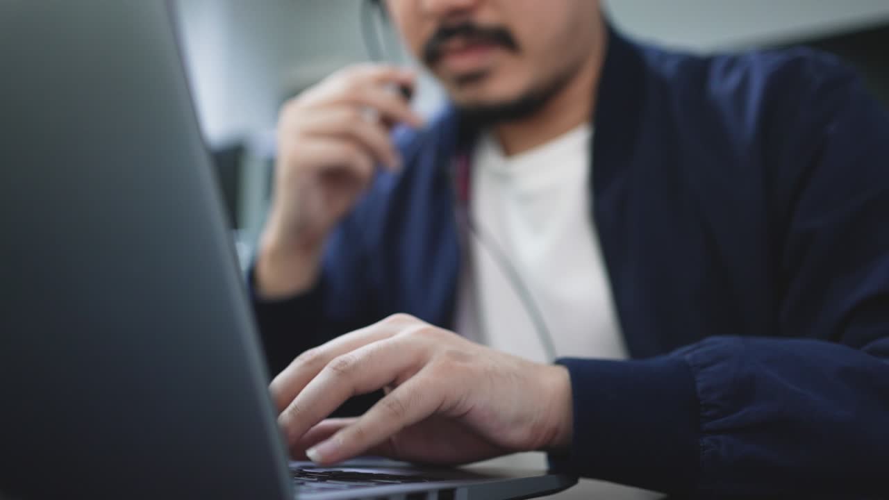 scena a rallentatore centro telefonico per adulti del medio oriente impiegato uomo tipo a mano sul portatile mentre parla con le cuffie con il cliente in ufficio di operazione per contattarci e concetto di lavoro di telemarketing