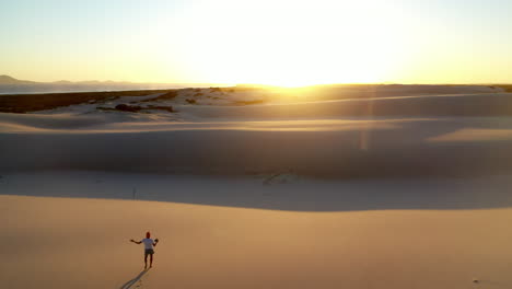 epic drone shot into the sun of a silhouetted man walking on sand dune