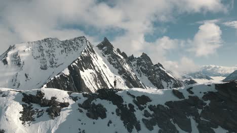 aerial footage of a person standing in front of a prominent peak in winter - südtiroler alpen