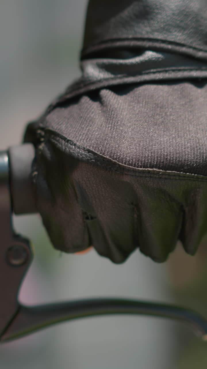 крупный план индивидуального рукоятки велосипеда с перчаткой на руке, дросселирование и удержание тормозного рычага, с солнечным светом, тонко отражающимся от перчатки, фон имеет мягкое размытие зелени