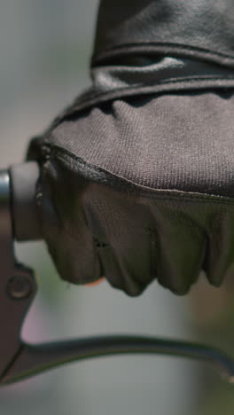 primer plano del manillar de la bicicleta individual con la mano con guante, acelerando y sosteniendo la palanca del freno, con la luz del sol sutilmente reflejada en el guante, el fondo presenta un suave borrón de vegetación