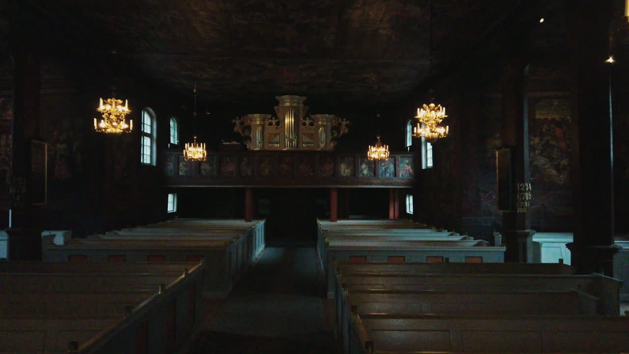 Dark interior view of empty and desolate pews, chandeliers and altar of historic Bottnaryd Church building, Bottnaryd, Sweden, covid-19 pandemic, Handheld pan left