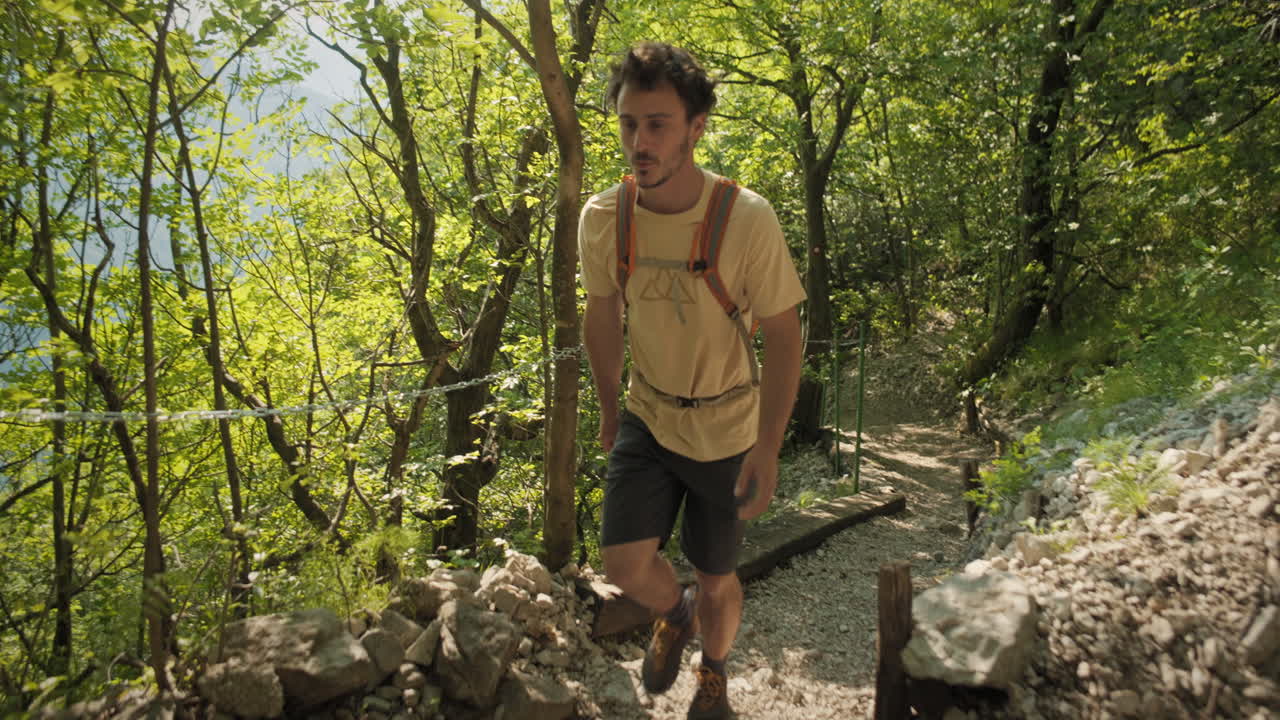 cámara rastreando a un excursionista con una mochila naranja usando ropa de verano caminando por un camino rocoso hacia el túnel excavado en la roca