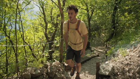 camera tracking a hiker with an orange backpack wearing summer clothes walking on a rocky path towards the tunnel carved into the rock